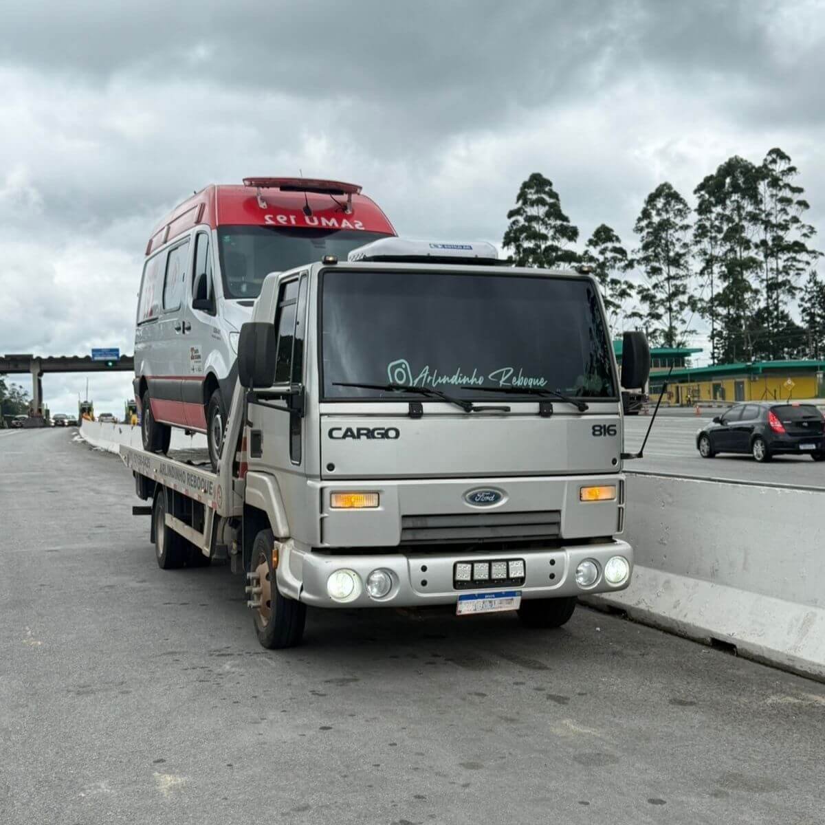 Caminhão guincho transportando van de Ambulância branca em rodovia de Mariana.