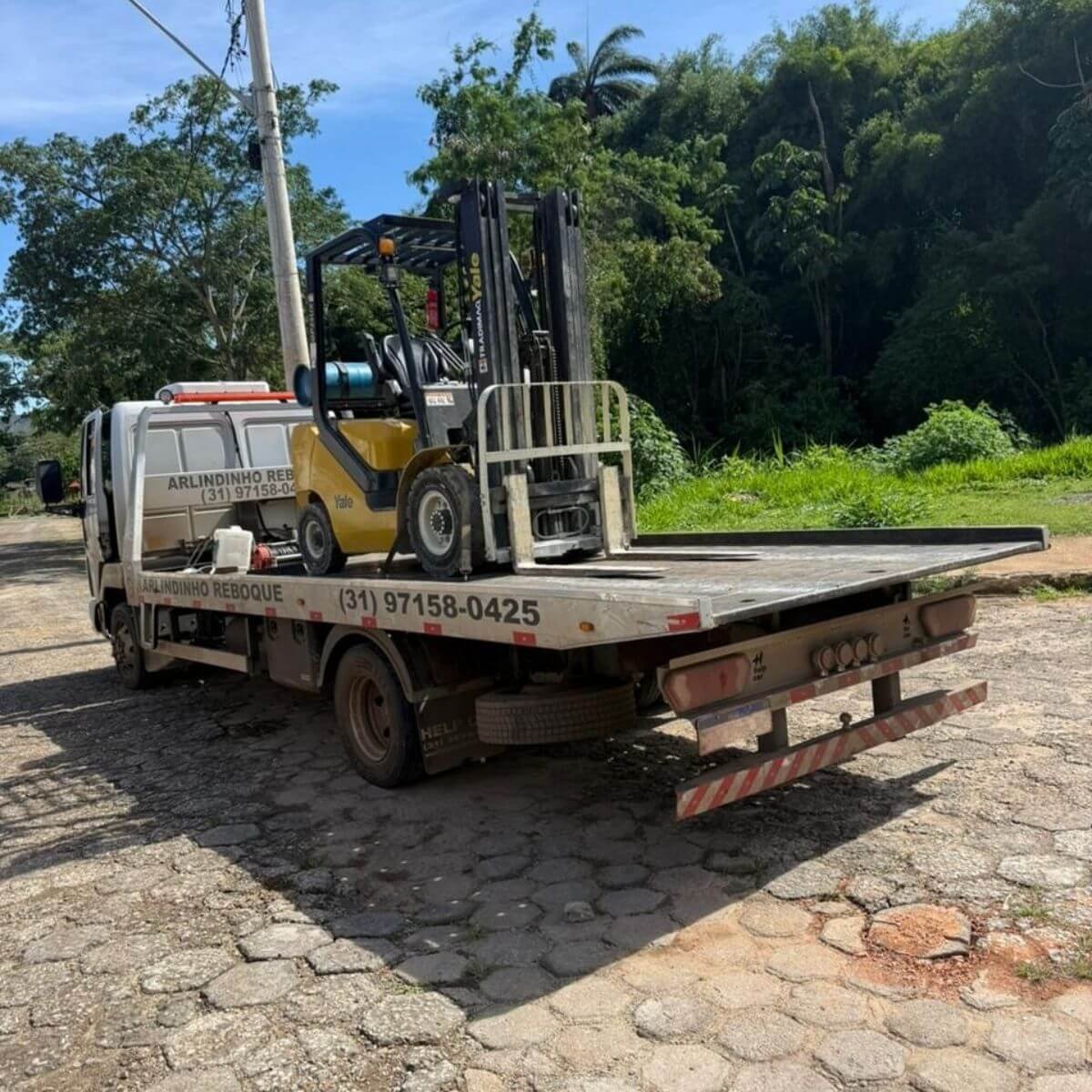 Transporte de equipamento industrial (empilhadeira amarela) em caminhão prancha.
