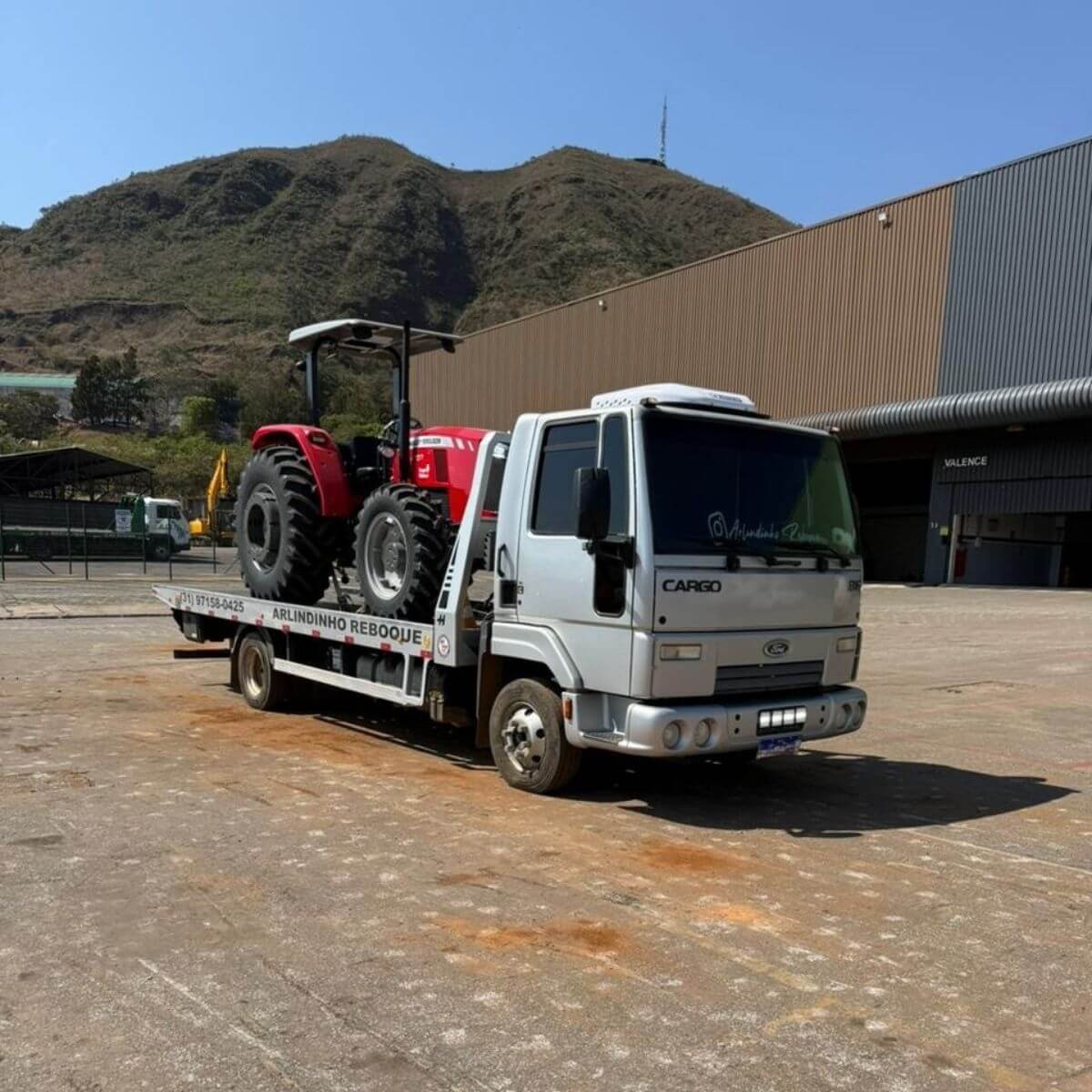 Guincho transportando trator vermelho grande para fazenda ou obra.